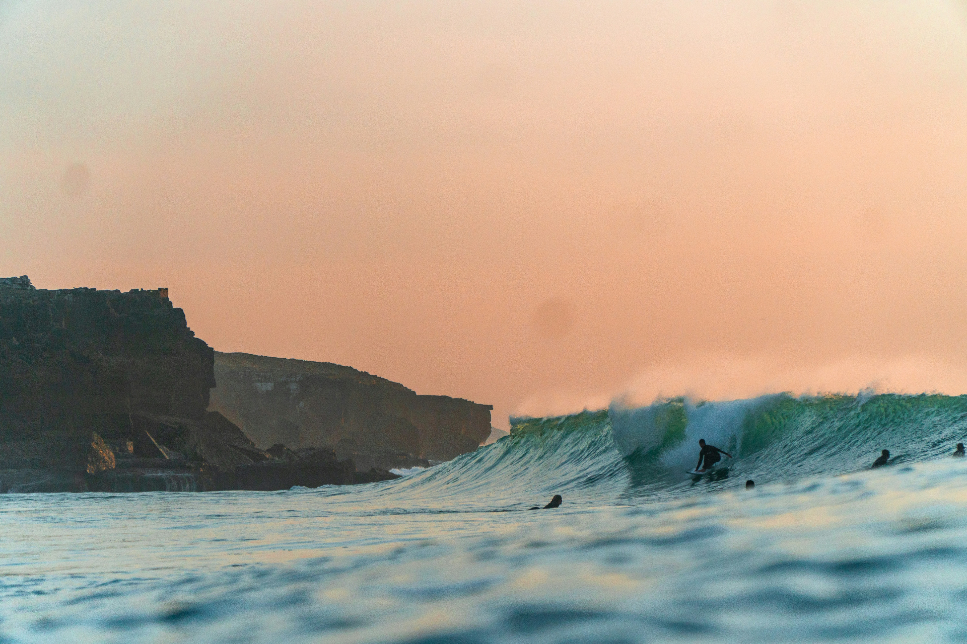 Surfers riding a powerful wave at sunset on the West Algarve coast